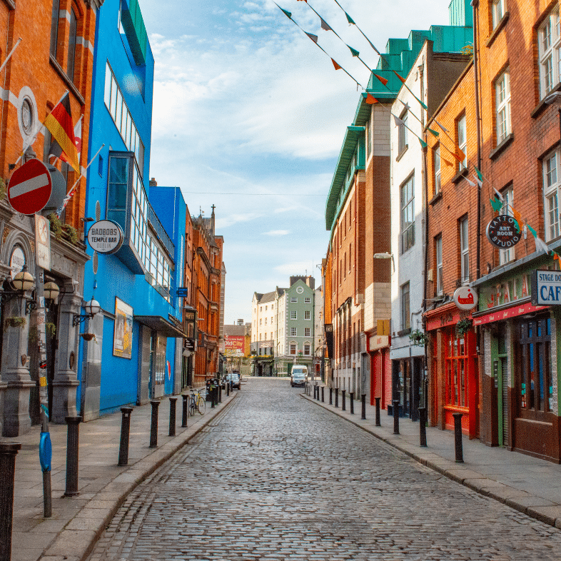 An image of Temple Bar, Dublin. The cobblestone street winds its way through the narrow alleys of the city, providing a scenic view of the outdoor infrastructure, buildings, and clouds in the sky.