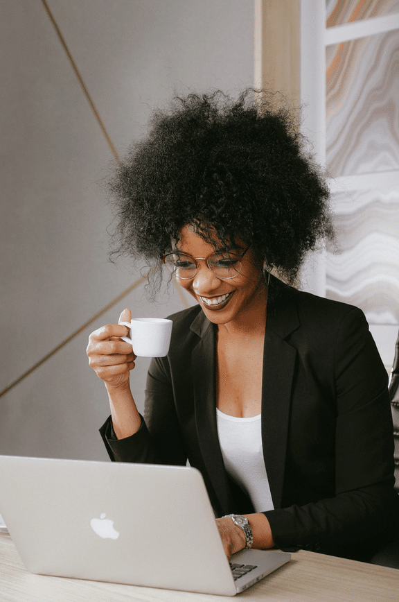 A woman in a business suit using a laptop and a cup of coffee.