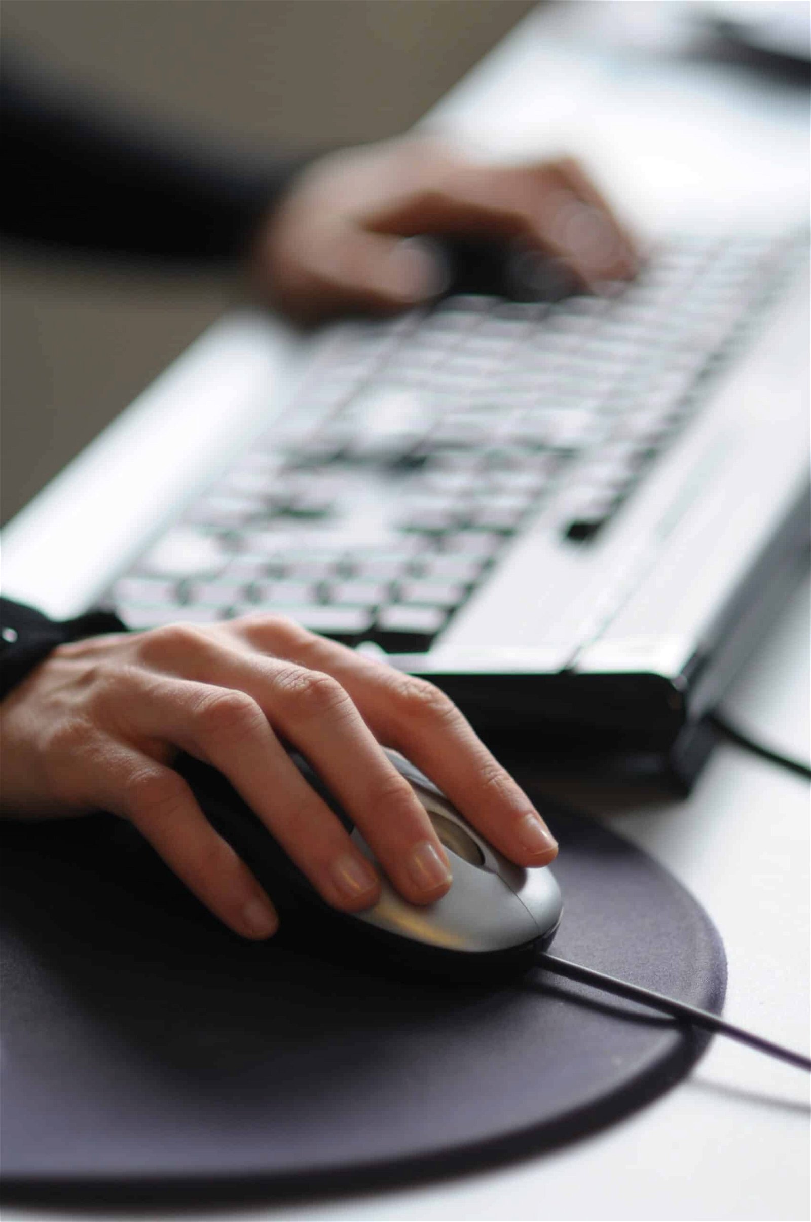 Close-up of a person's hand using a computer mouse with a keyboard in the background.