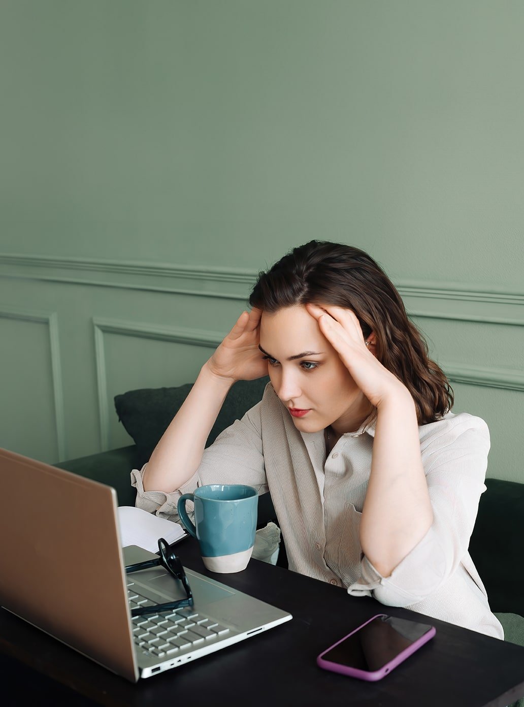 A woman looks focused and stressed while working on a laptop at a desk with a smartphone and troubleshooting top WordPress issues beside her.