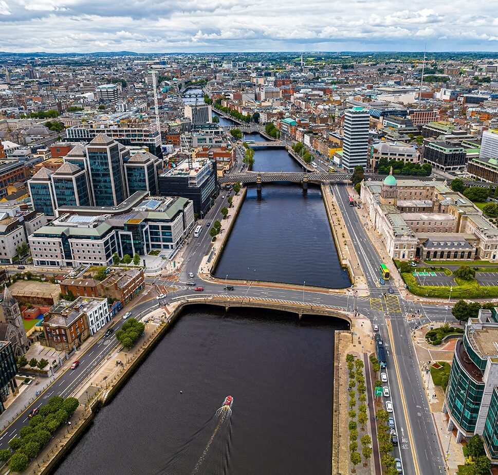Aerial view of Dublin hosting a cityscape featuring a river flowing through, surrounded by modern buildings and bridges, under a cloudy sky.